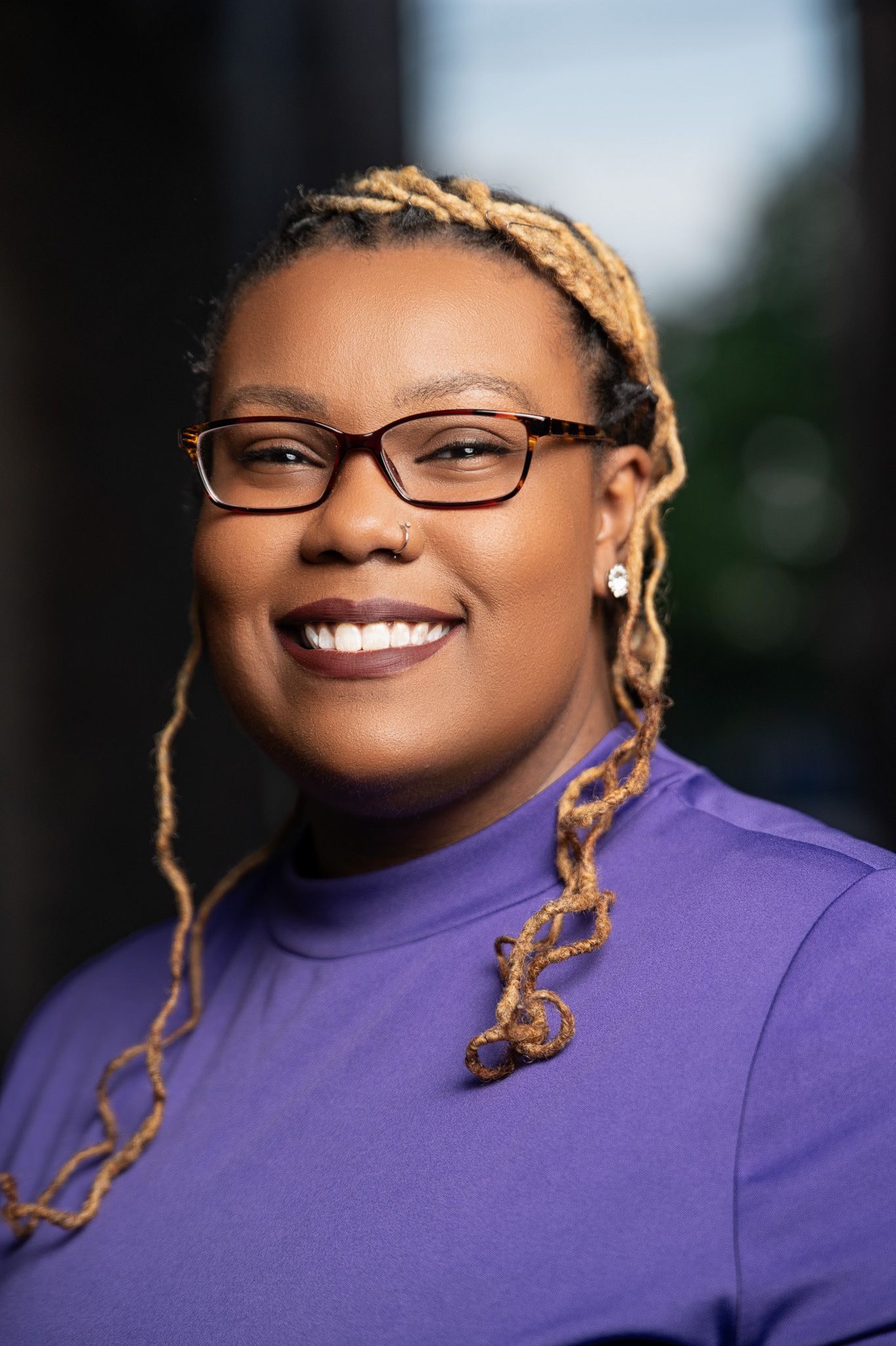 A person wearing glasses and a purple top smiles warmly in a series of four outdoor portrait shots.