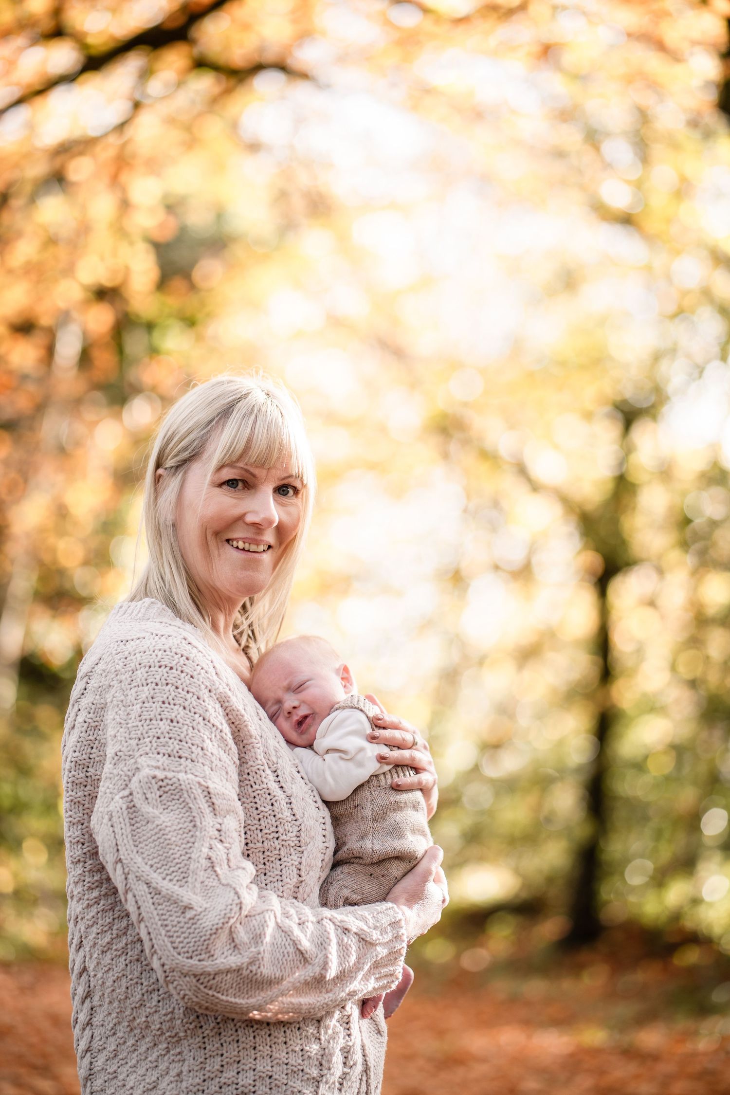 A person wearing a cozy beige sweater holds a warm drink outdoors during autumn with golden bokeh background.