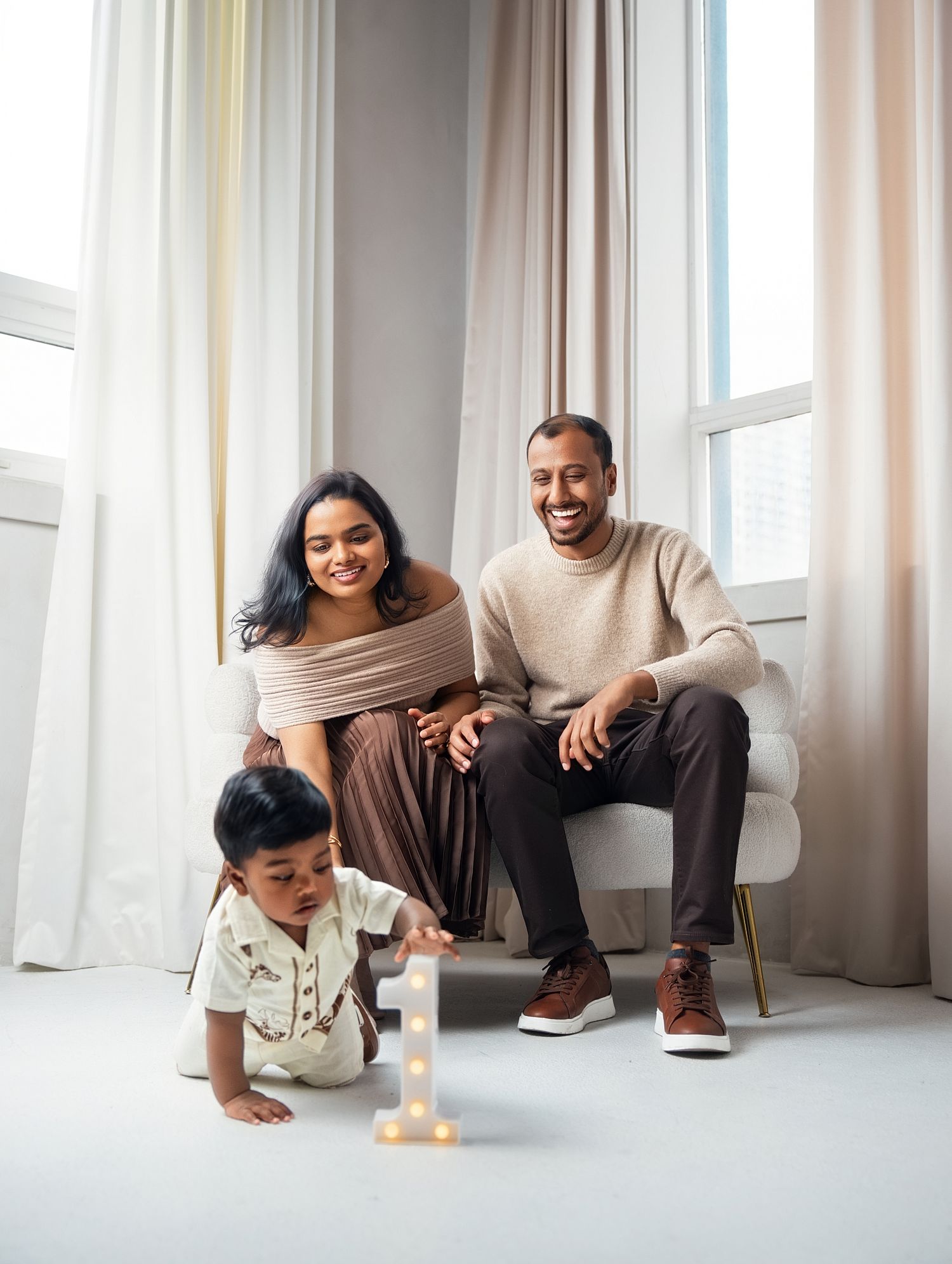Family portrait of parents holding baby girl in pink dress in a studio setting.
