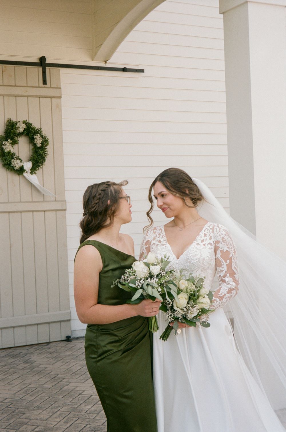 Two people share an emotional moment in formal attire at an elegant white-columned venue with decorative wreaths.