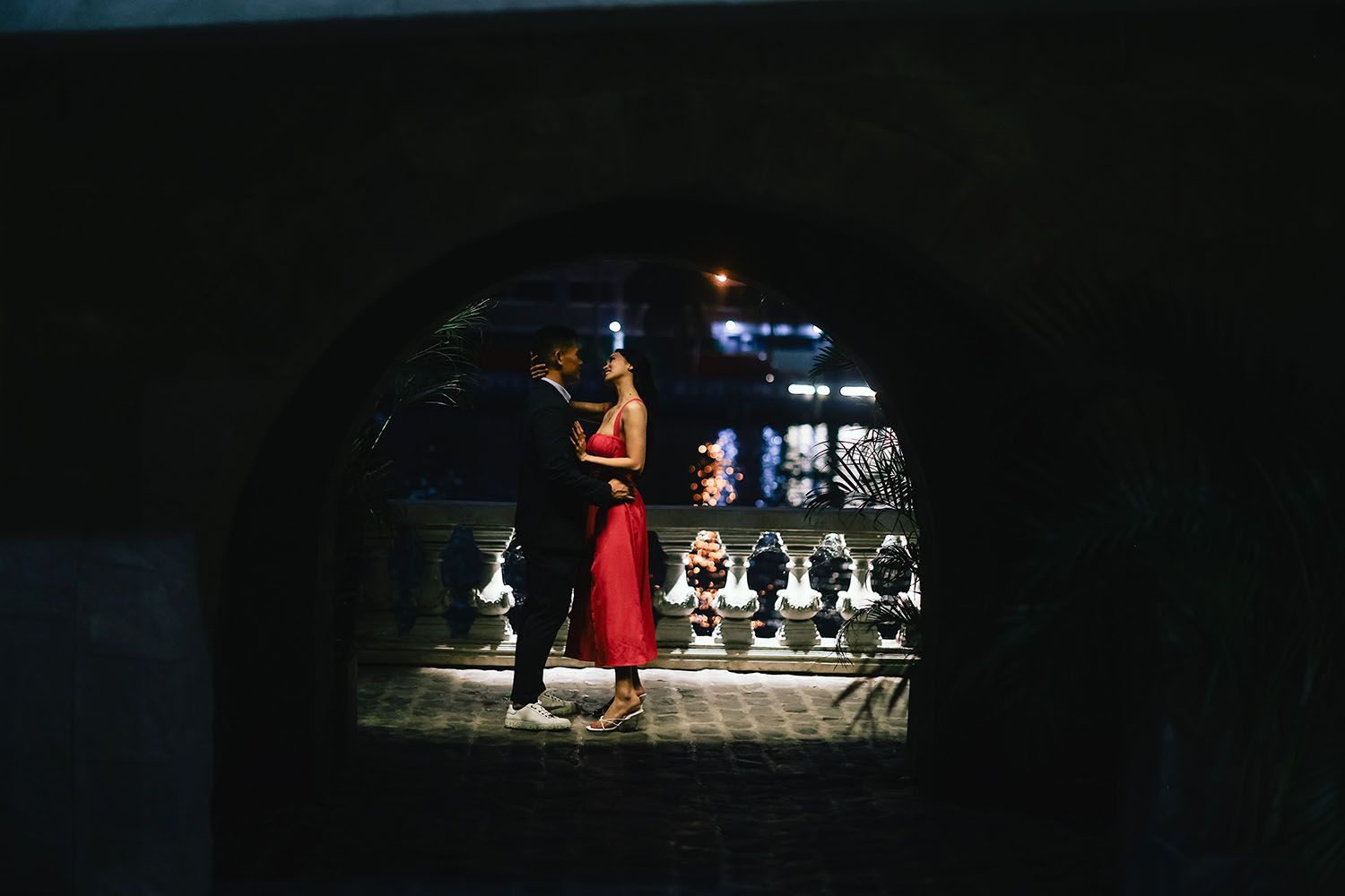 A person in a red dress stands silhouetted against a dark background with illuminated white chairs in the distance.