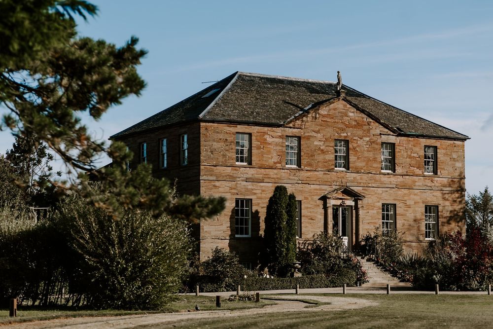 Historic sandstone buildings from the colonial era stand in a row against a blue sky and green trees.