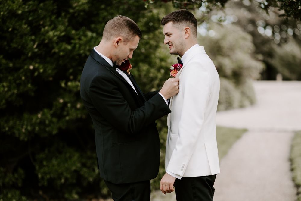 A touching moment between two grooms on their wedding day as one adjusts the other's boutonniere.