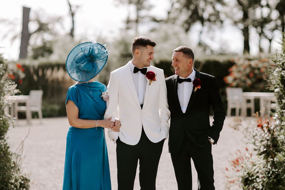 Wedding party members in formal attire gather outdoors for candid moments at an elegant garden venue.