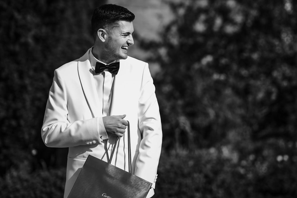 A person in a white tuxedo jacket poses outdoors in a black and white photograph.