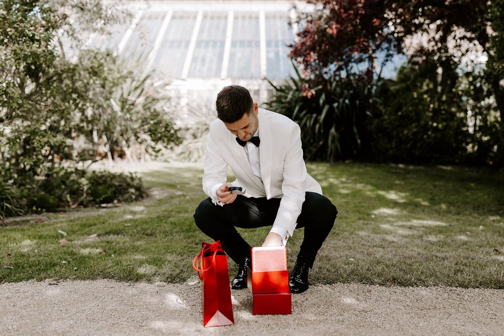 Wedding guest signing a red guestbook on an outdoor table during a garden ceremony.