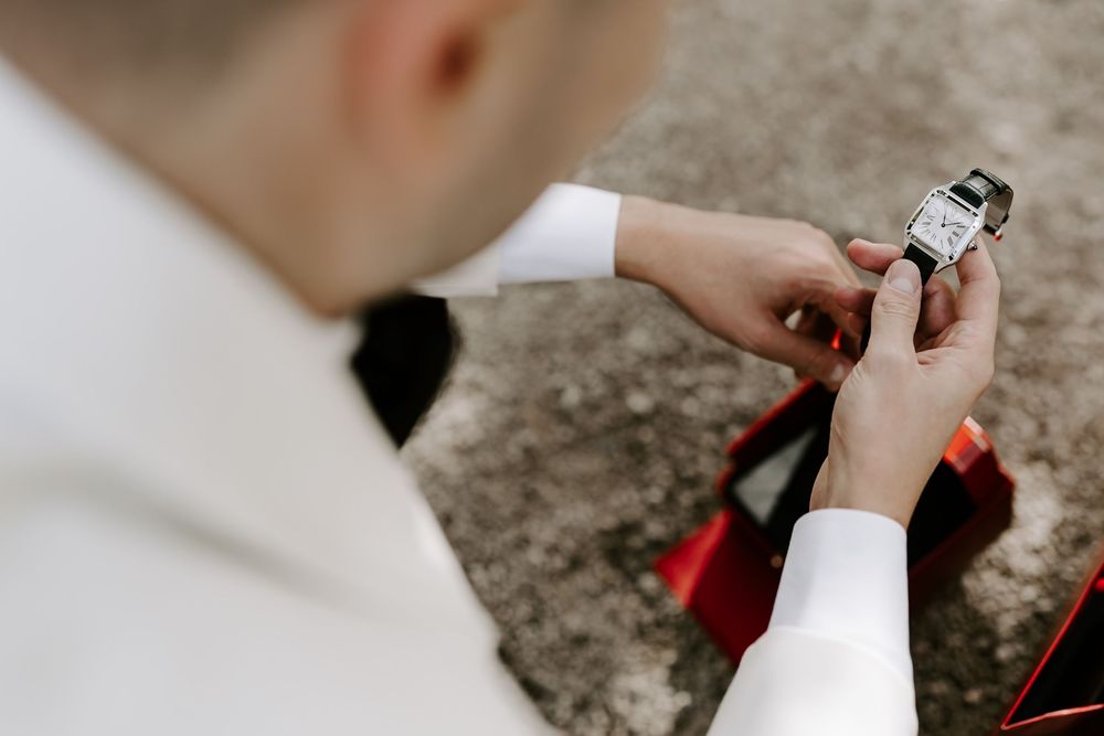 Hands delicately tying a red bow tie around a formal white collar during wedding preparation.