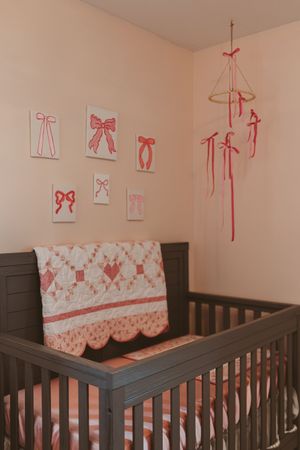 Dark wood crib with pink bow decorations and matching bedding in nursery.