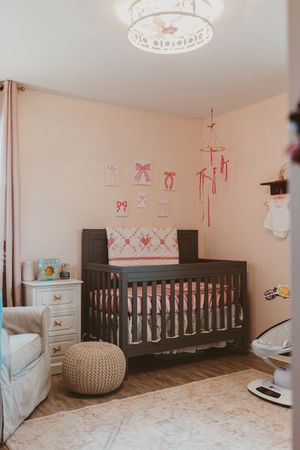 Spacious nursery room with dark wood crib, crown light fixture, and pink decorative accents.