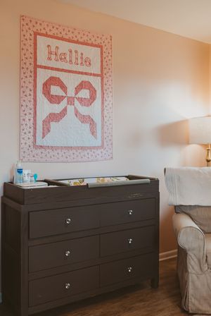 Dark wood dresser with pink bow artwork displayed above in nursery.