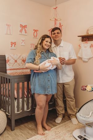 Family moment in nursery with crib and pink bow decorations.