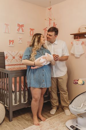 A nursery room decorated with pink bow accents features a dark gray crib and intimate family moment.