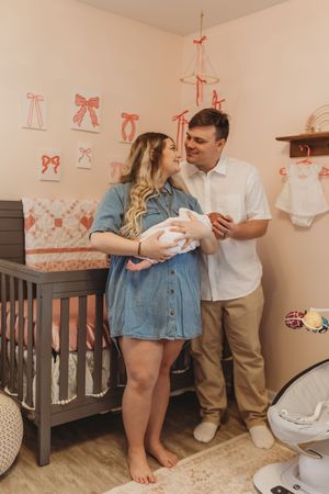 A cozy nursery scene with pink wall decorations and a dark wooden crib in the background.