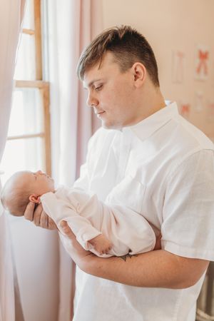 A tender moment with a newborn baby swaddled in white being cradled gently.