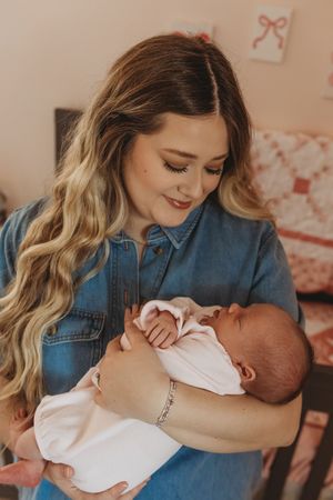 A tender nurturing moment with a sleeping newborn baby dressed in white.