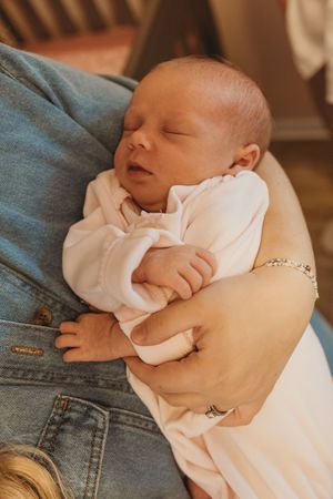 A sleeping newborn baby in white clothing rests peacefully against denim.