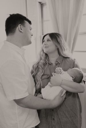 A tender family moment as new parents gaze lovingly at each other while holding their newborn baby in a sunlit room.