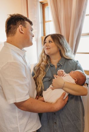 A heartwarming scene of parents sharing an intimate moment while cradling their newborn baby near a window.