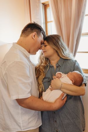 An intimate family portrait showing parents sharing a close moment while holding their sleeping newborn.