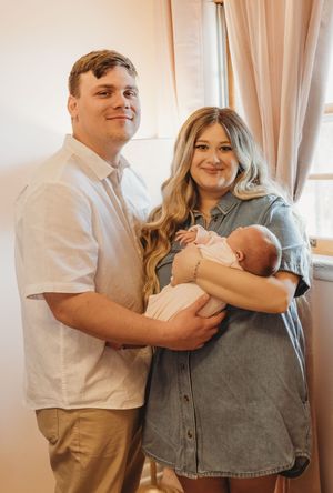 A sweet family portrait in a sunlit room as parents proudly hold their newborn baby.