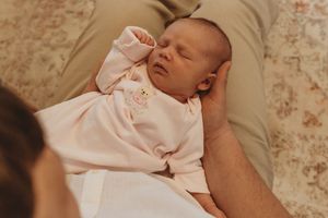 A peaceful sleeping newborn baby wearing a light pink outfit rests on a patterned surface.