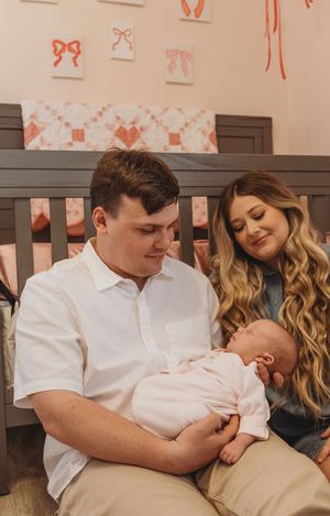 A tender nursery scene with decorative wall art as parents bond with their sleeping newborn.