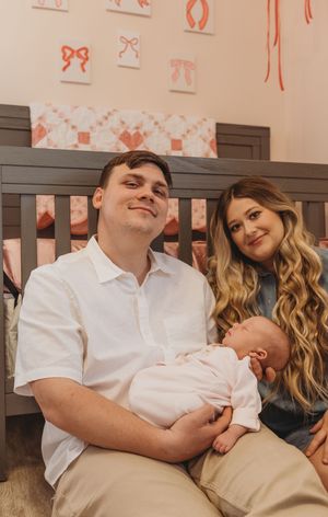 A tender family moment in a nursery with pink bow decorations on the wall.