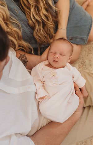 Baby wearing soft pink outfit rests peacefully in parent's arms.