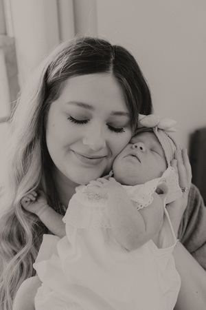 Four black and white photos showing gentle interactions with a baby wearing a white outfit.