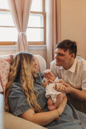 Candid family photos capturing playful moments with a newborn on a beige couch by a window.