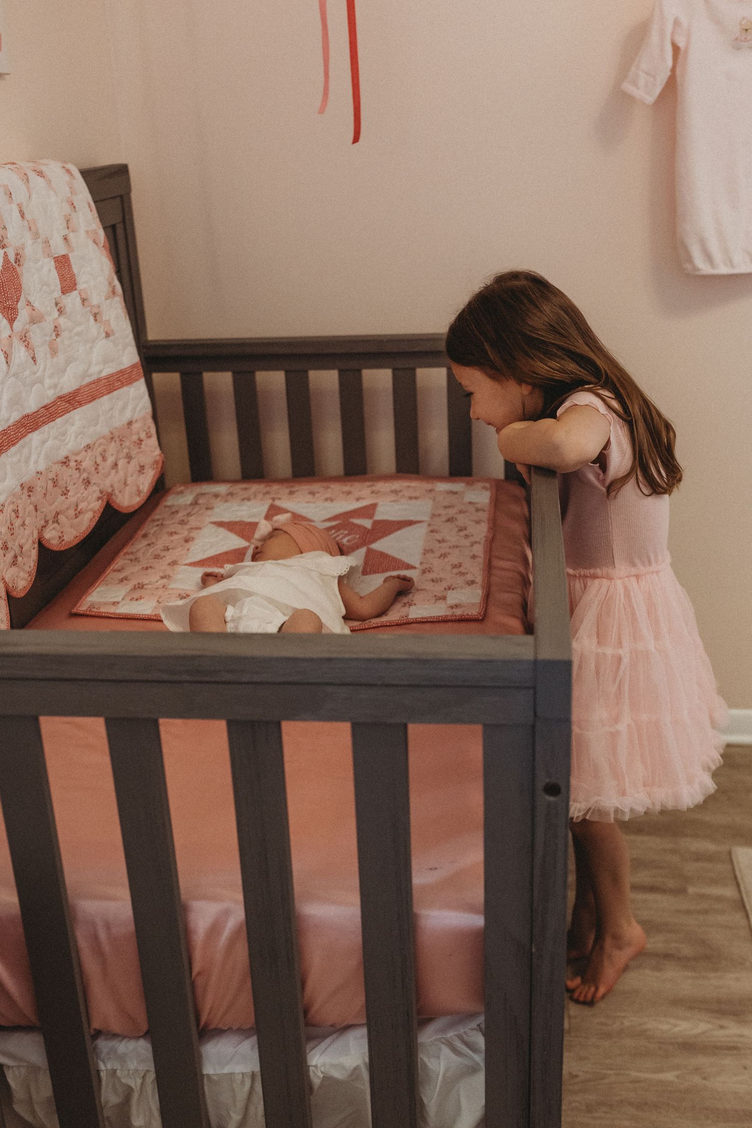 Dark wooden crib with pink bedding and floral patterns in a nursery setting.