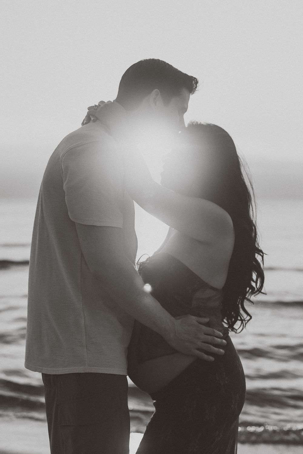 A romantic black and white photo series showing a couple embracing on a beach at sunset.