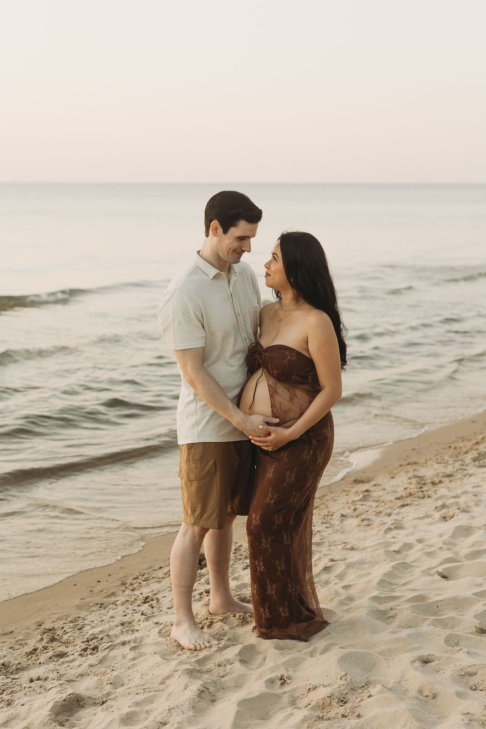 A couple embraces on a sandy beach at sunset while waves roll in along the shoreline.