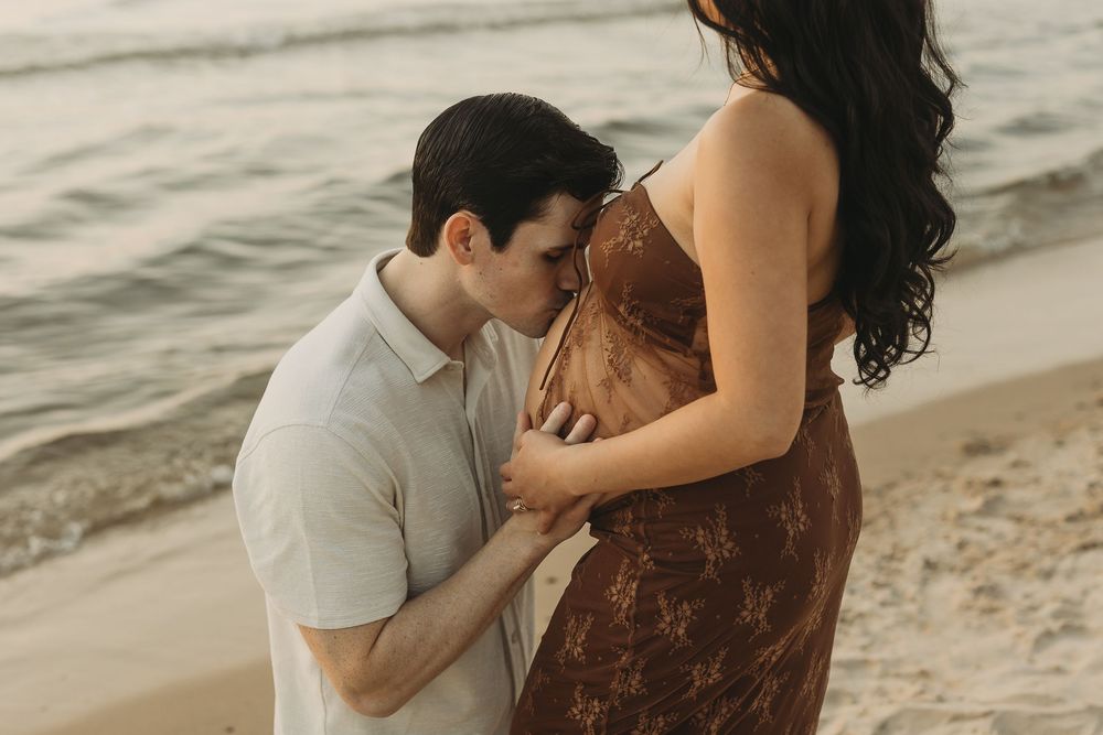 Romantic couple sharing intimate moments on a sandy beach during sunset with waves in the background.