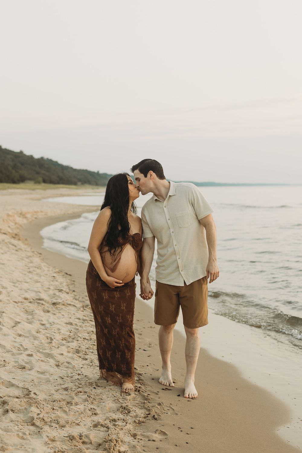 A romantic couple walks together along the shoreline during golden hour at the beach.