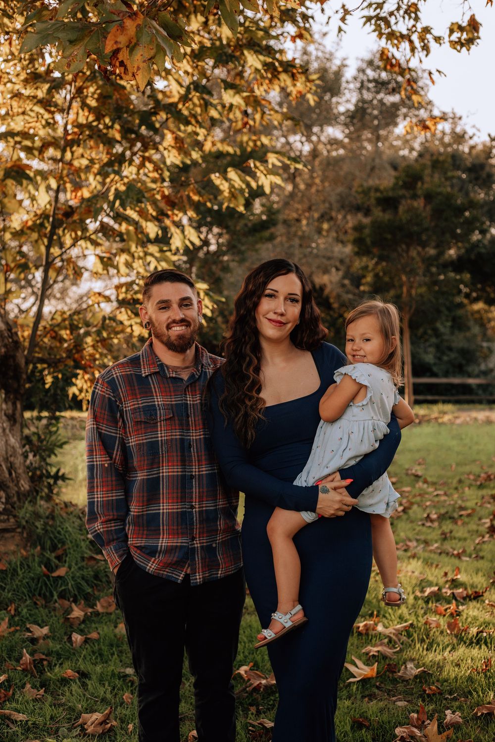 A family shares joyful moments together outdoors during a fall photoshoot with golden sunlight.