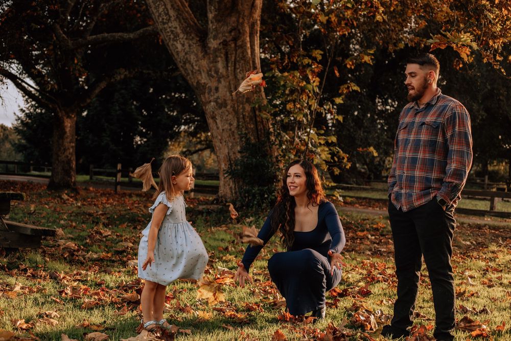 A group stands together in a sunlit autumn park with golden leaves scattered on the ground during a fall photoshoot.