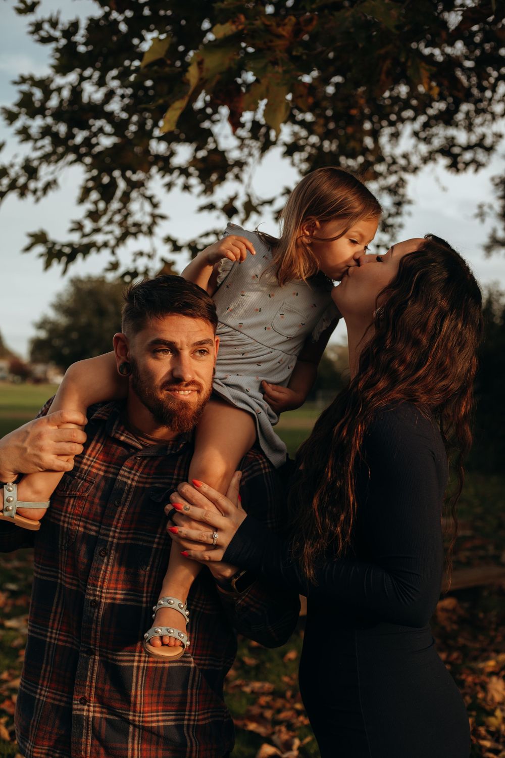Playful family photoshoot moments captured in a park with autumn trees in the background.