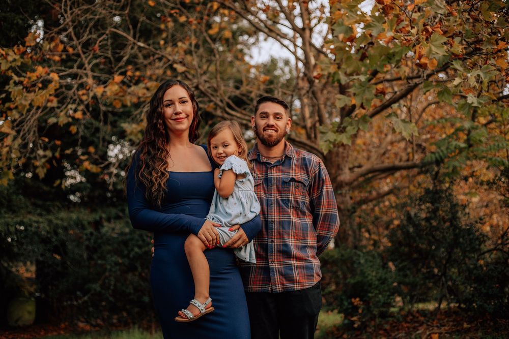 Family enjoying a warm autumn day together in a park with golden fall foliage in the background.