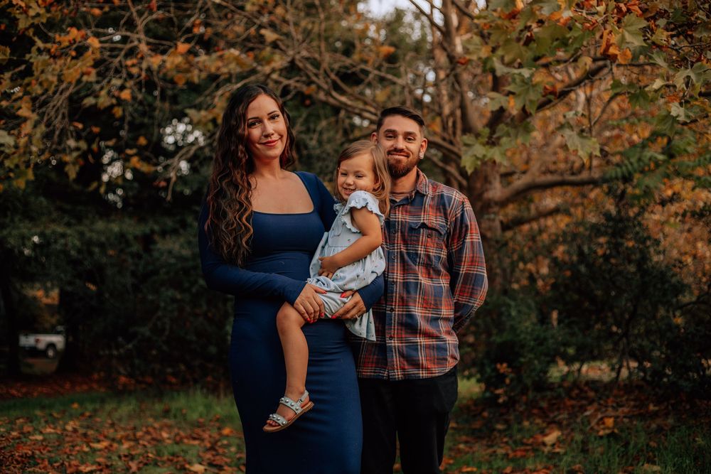 Family poses together during autumn photo session with warm fall foliage in background.