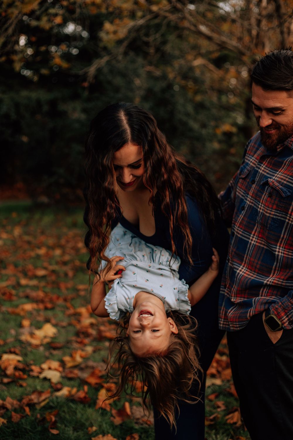 Playful family moment captured in fallen autumn leaves during sunset.
