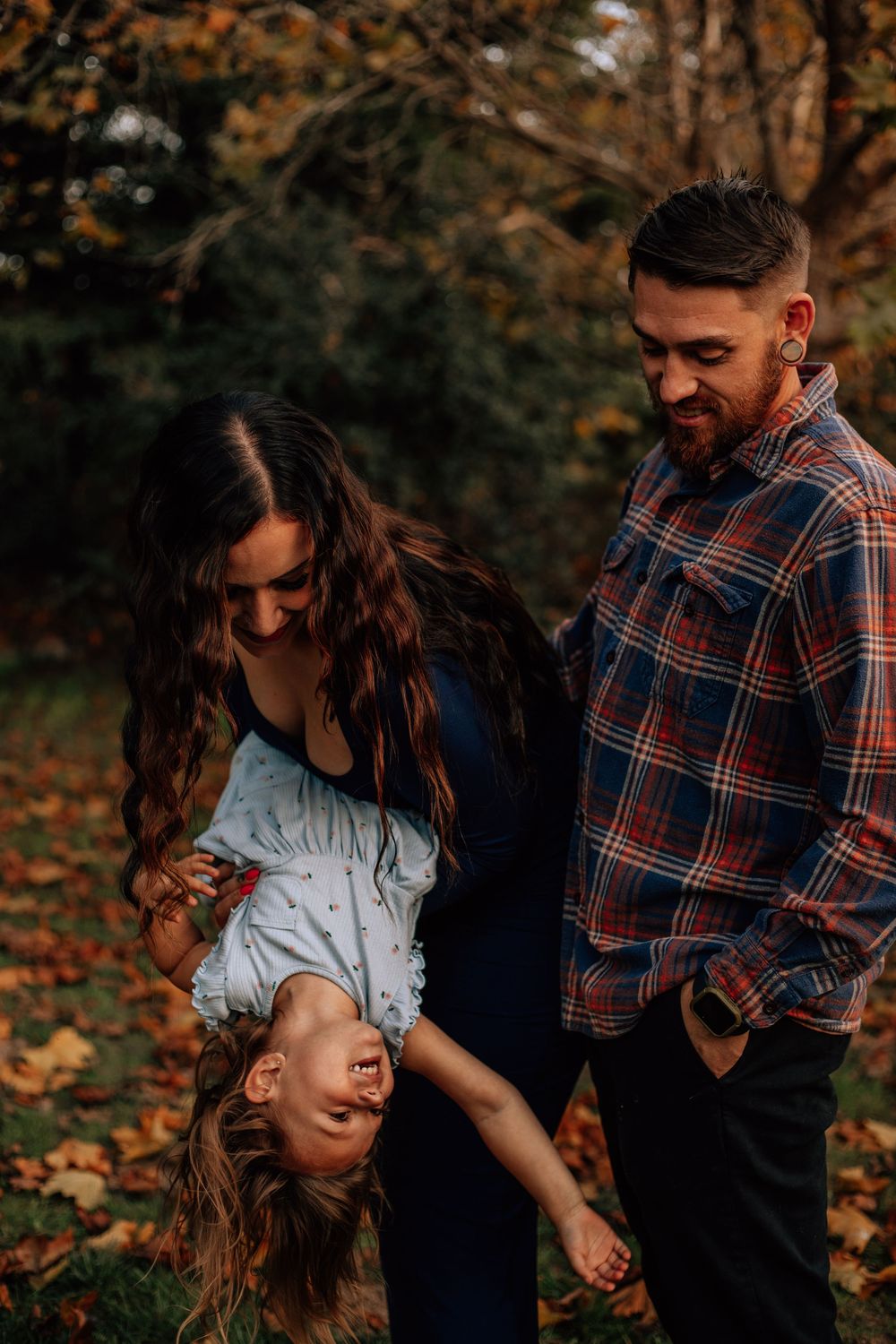 A playful family moment captured in warm autumn lighting with fallen leaves around them.