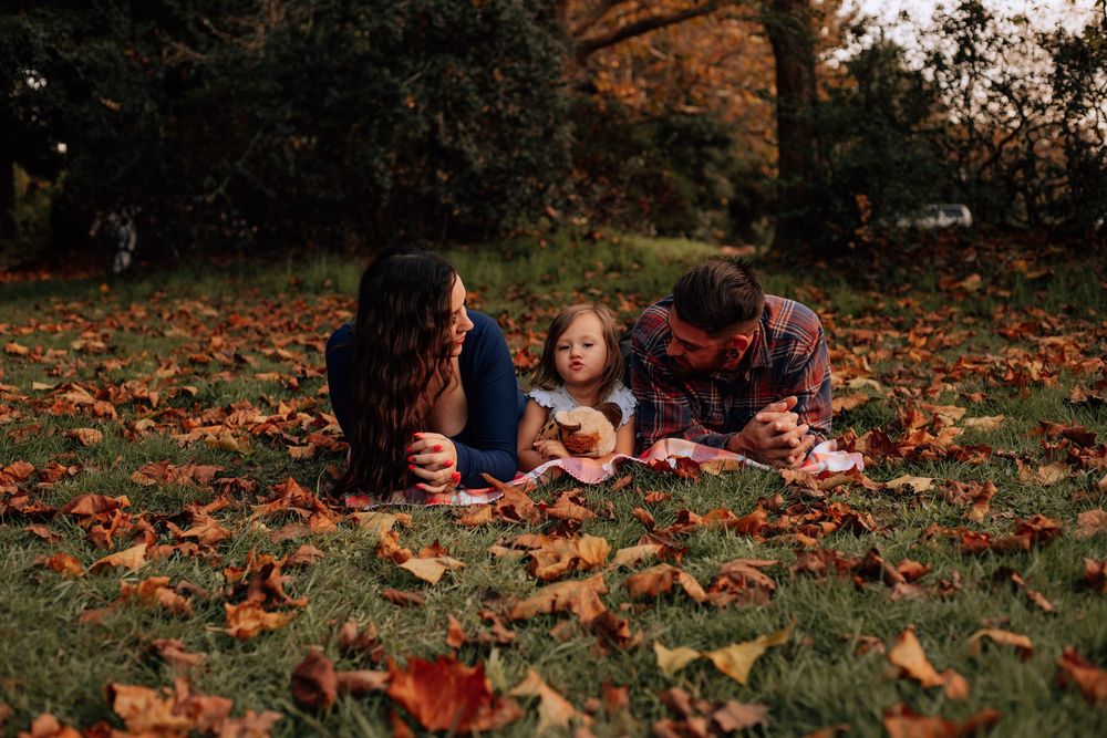 Family enjoys quality time together on grass covered with fallen autumn leaves at dusk.