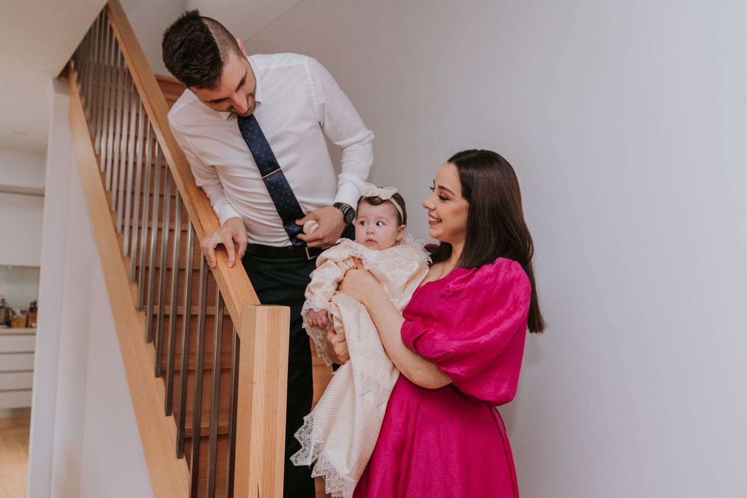 Family shares a joyful moment together on the staircase with parent in pink dress holding a baby.