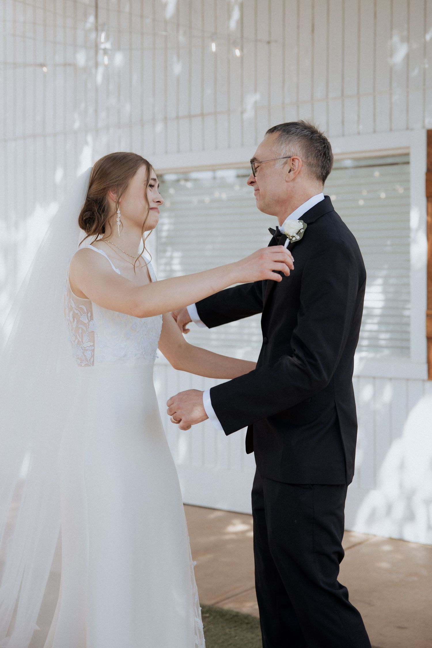 A bride and father share an emotional first dance together in a bright, sunlit reception venue.
