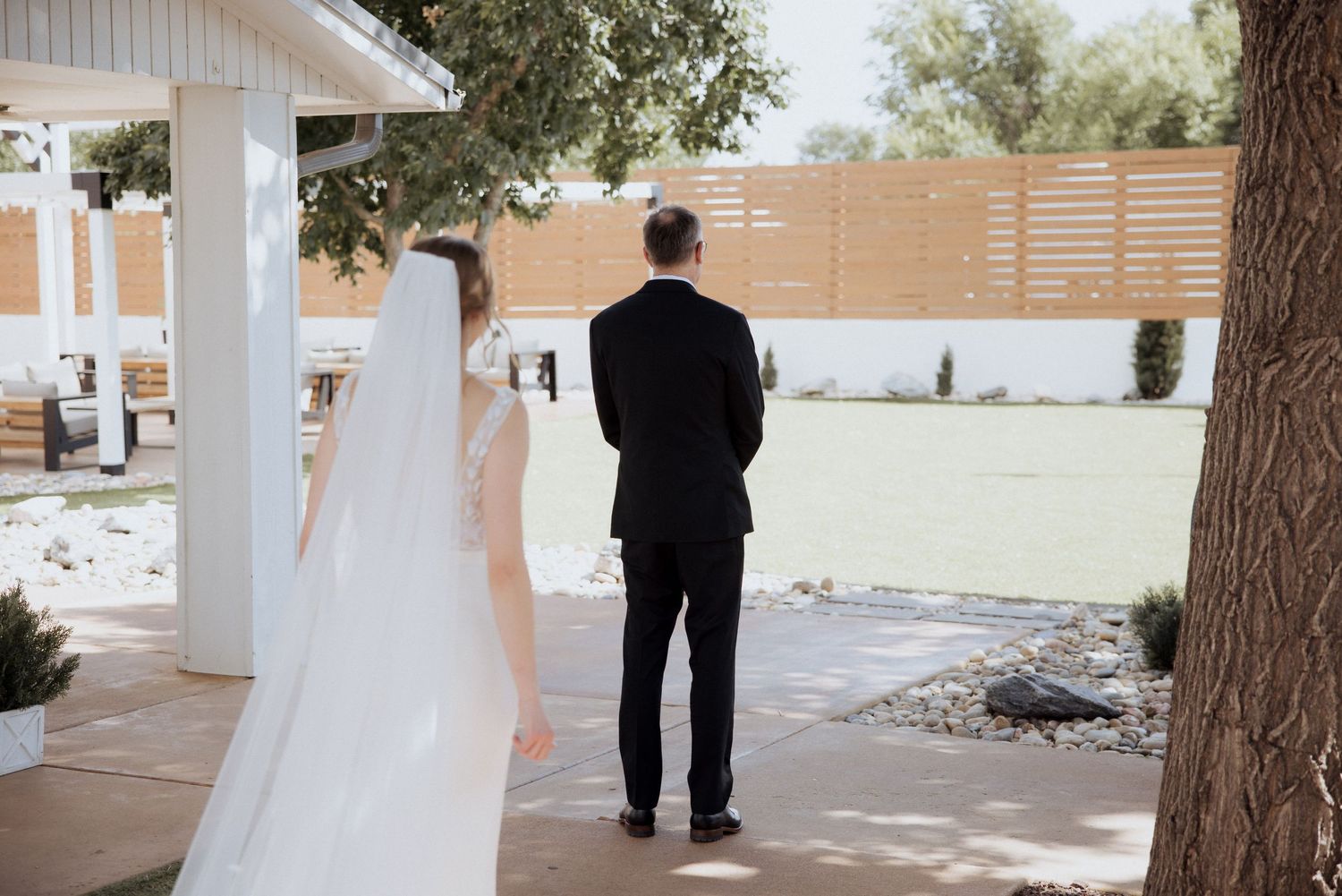 A bride and groom walk together down a covered outdoor walkway decorated with hanging floral arrangements.
