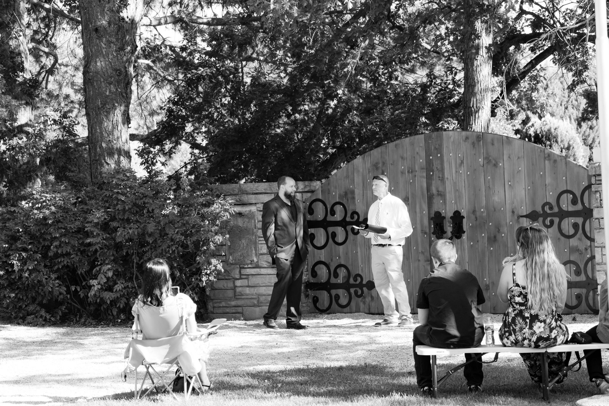 A black and white photo of a wedding ceremony in front of a decorative wooden gate with ornate details.