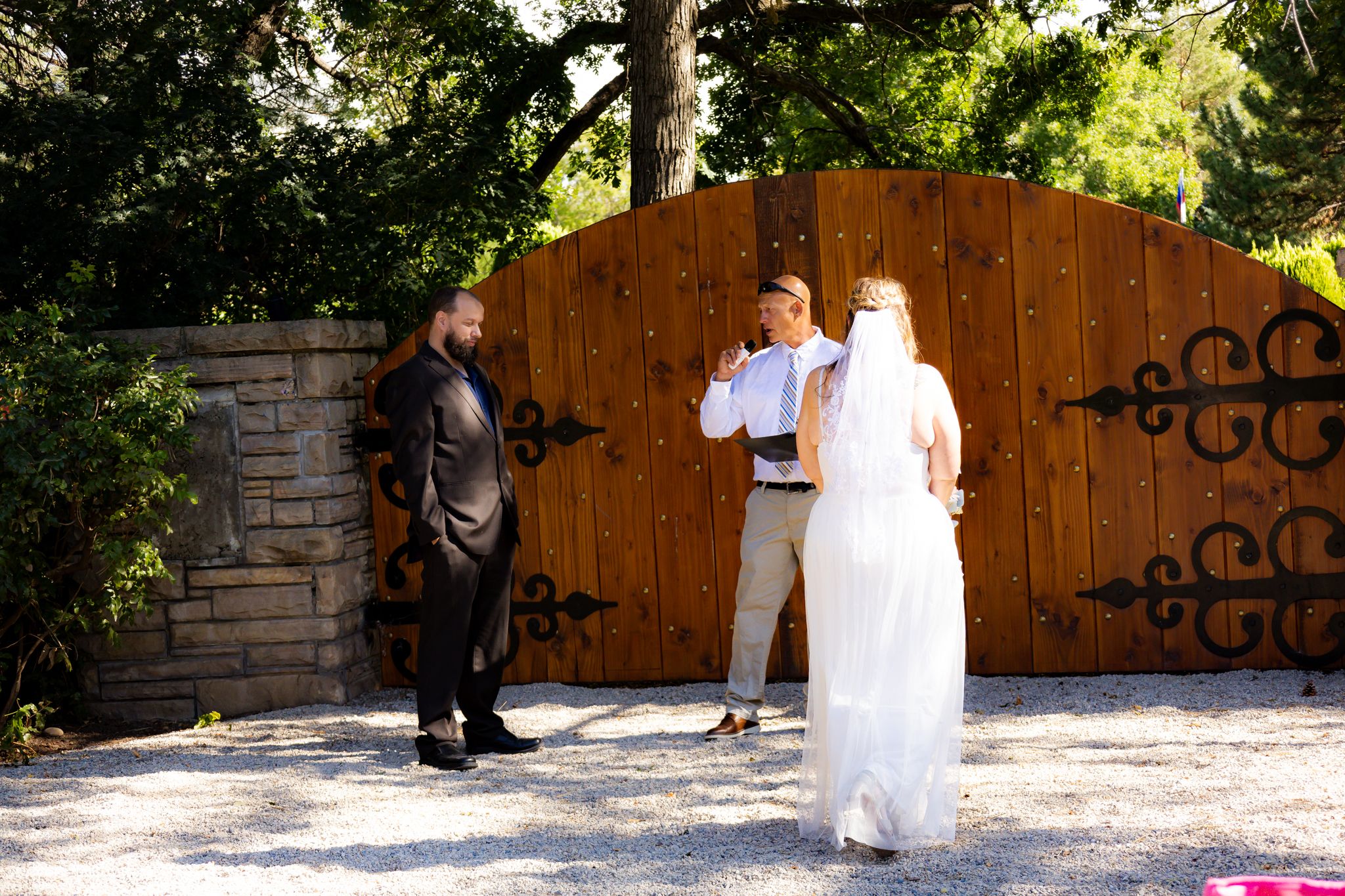A wedding ceremony taking place in front of a large wooden gate with decorative iron scrollwork.