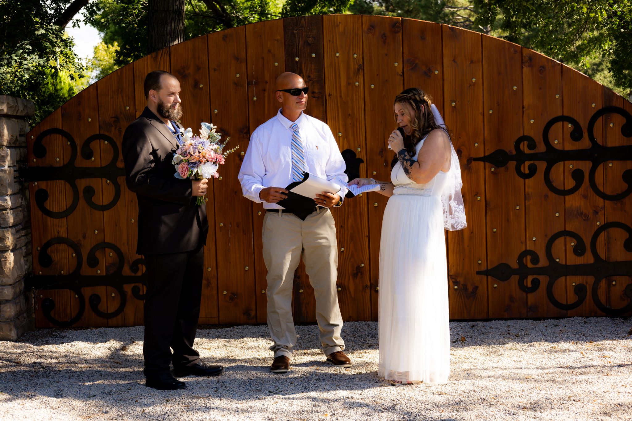 A small wedding ceremony in progress in front of a wooden gate with black decorative details.