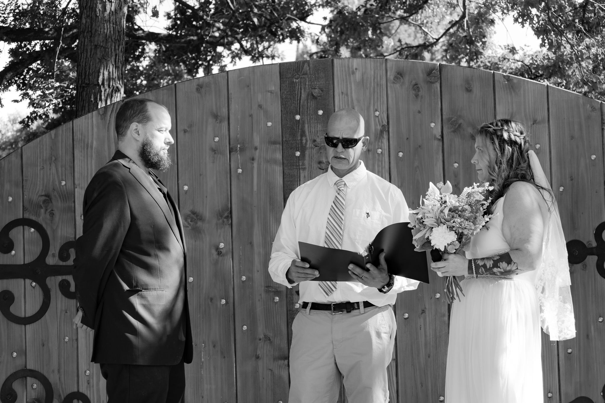 A black and white capture of an intimate wedding ceremony against a wooden gate backdrop.